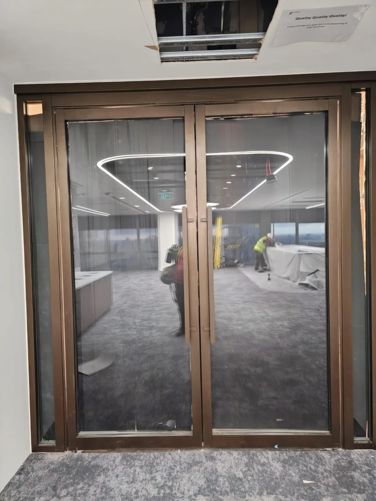 Completed glazed bronze-framed double doors, with feature ceiling detail and city views beyond.