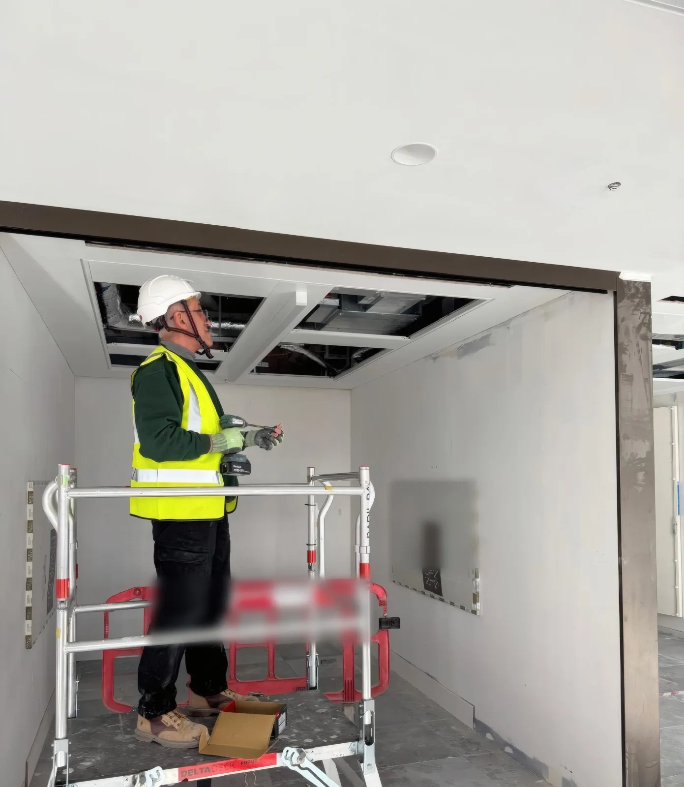 An OMFC International installer completing overhead works to a partition head from a podium platform.