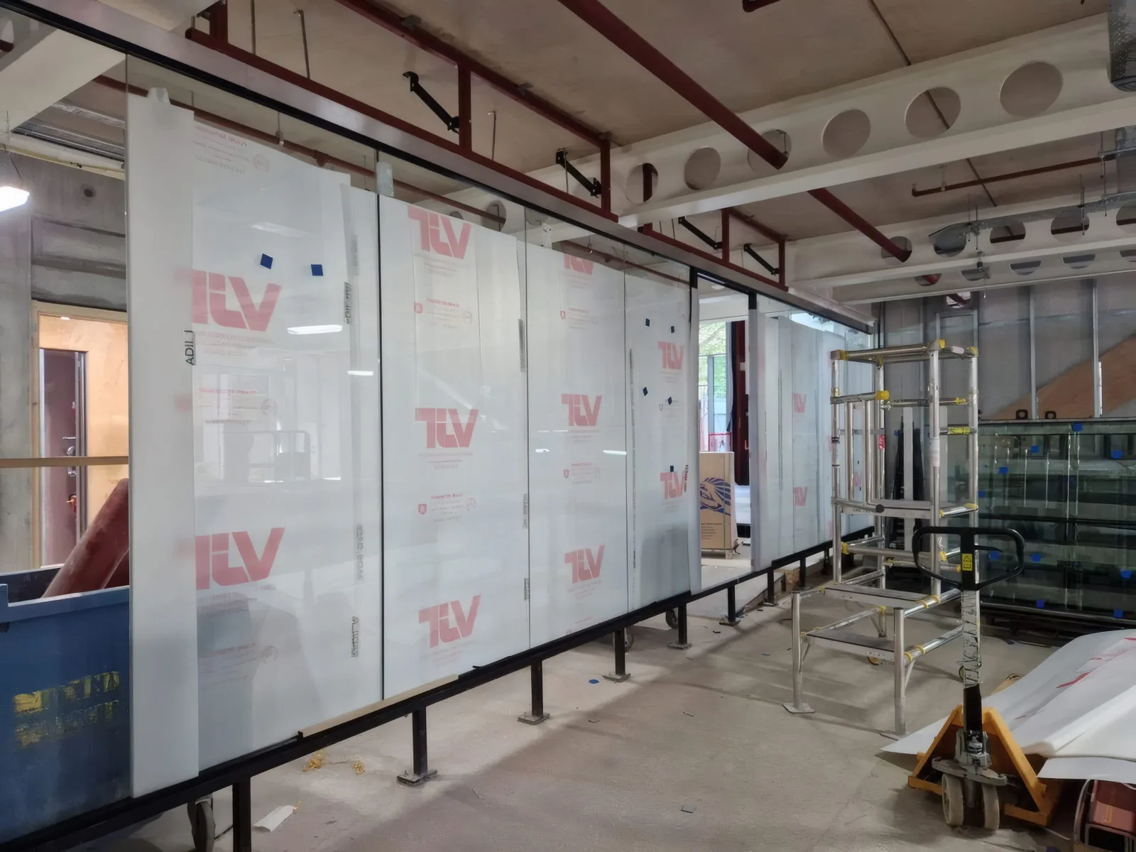 A completed run of glazed screen panels, still in protective film, spanning the full width of the workspace.