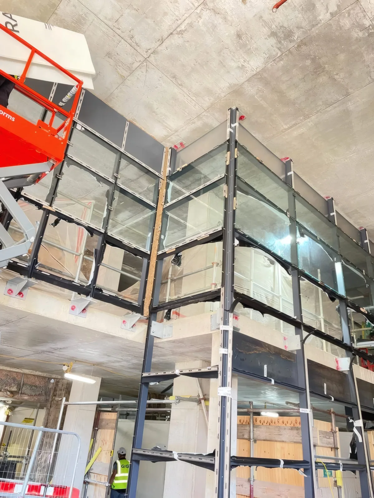 A two-storey glazed corner in the atrium, framed and glazed, with a MEWP at its head.