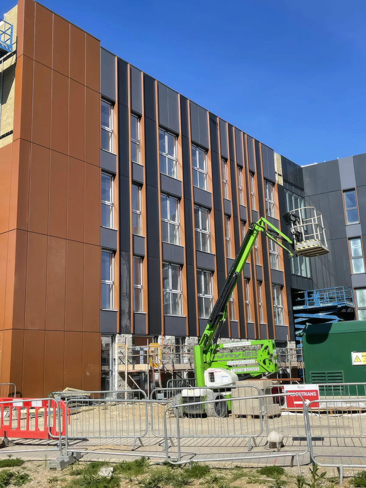 The copper-coloured corner and dark vertical panels, with a boom lift at work.