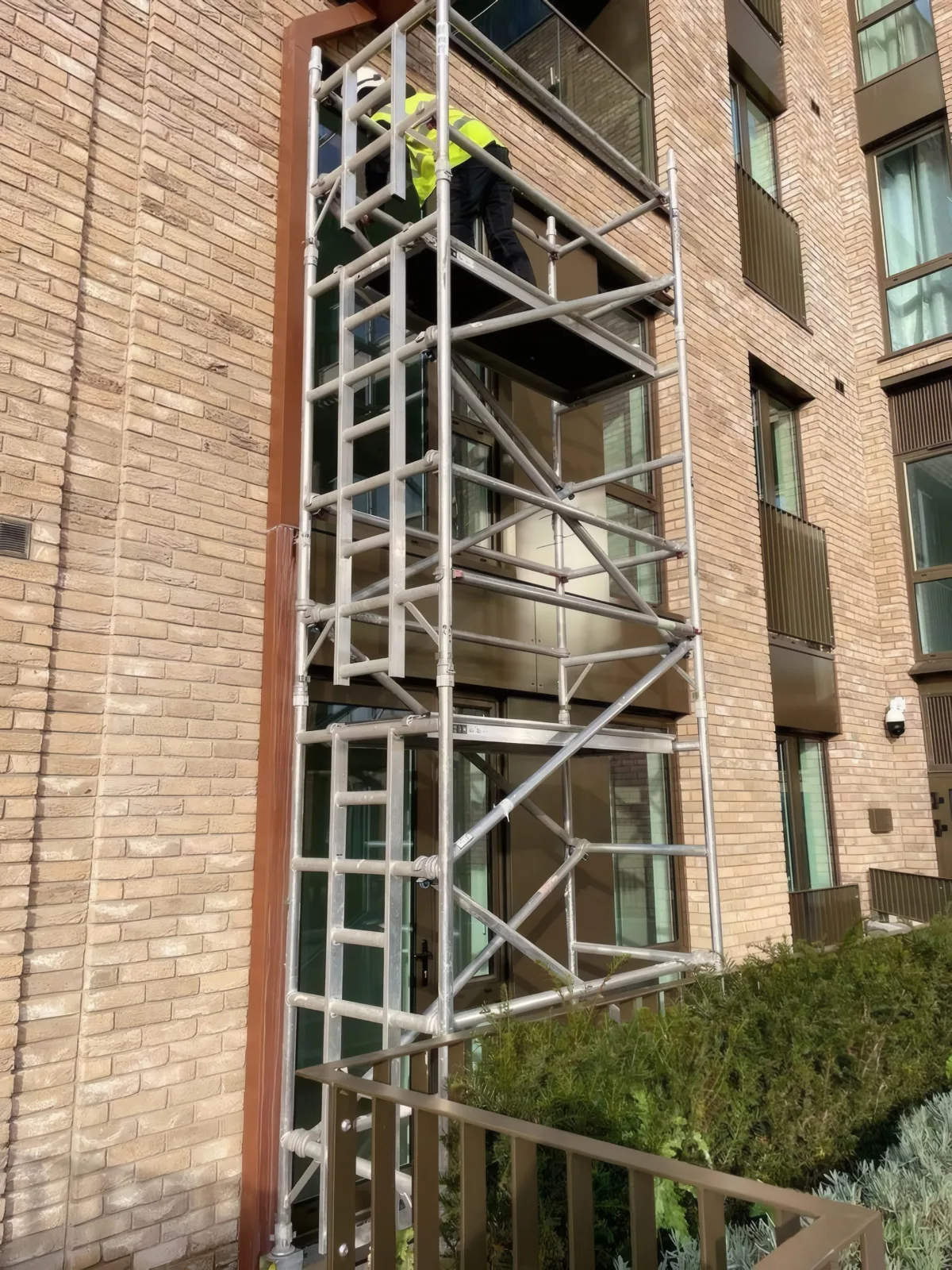A mobile access tower positioned against the brick facade during balustrade and cladding installation.